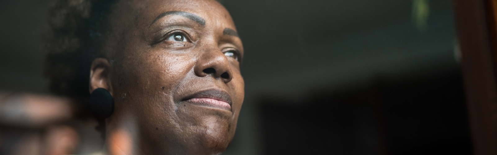 A middle-aged Black woman looks thoughtfully out of the window