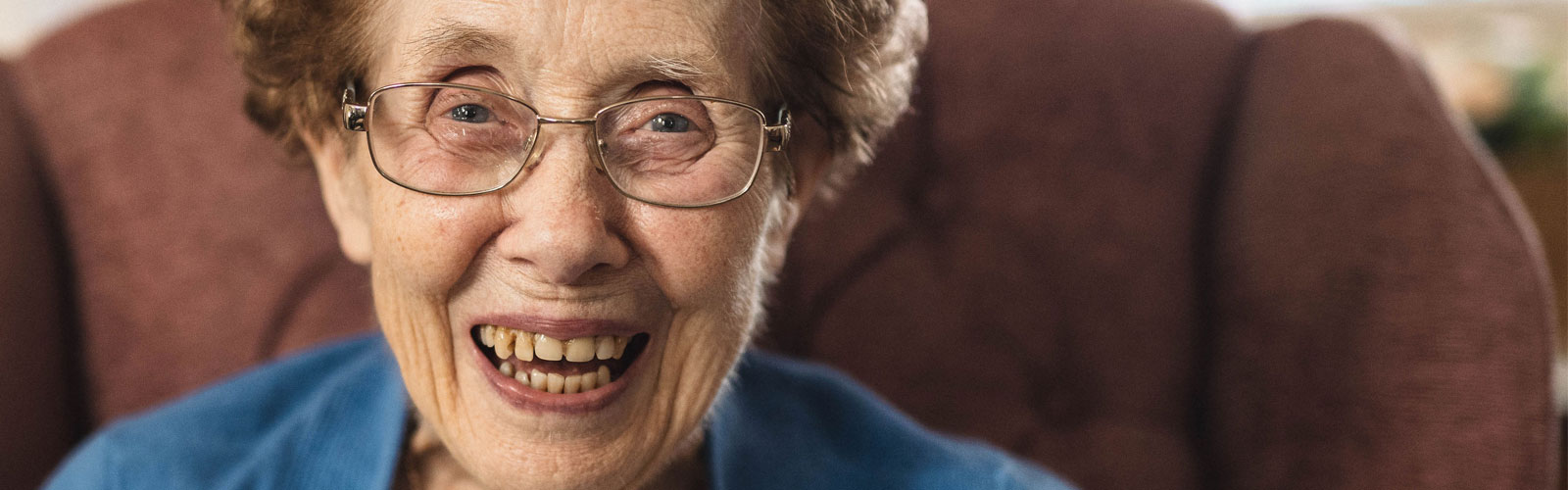 An older lady with glasses, smiles into the camera