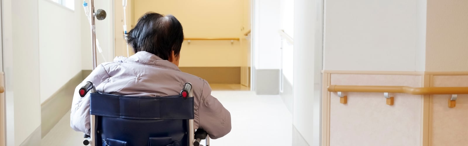 An older person waits in a hospital corridor in a wheelchair, alone