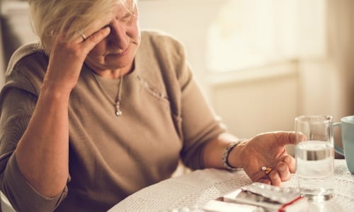 An older woman taking tablets and looking confused