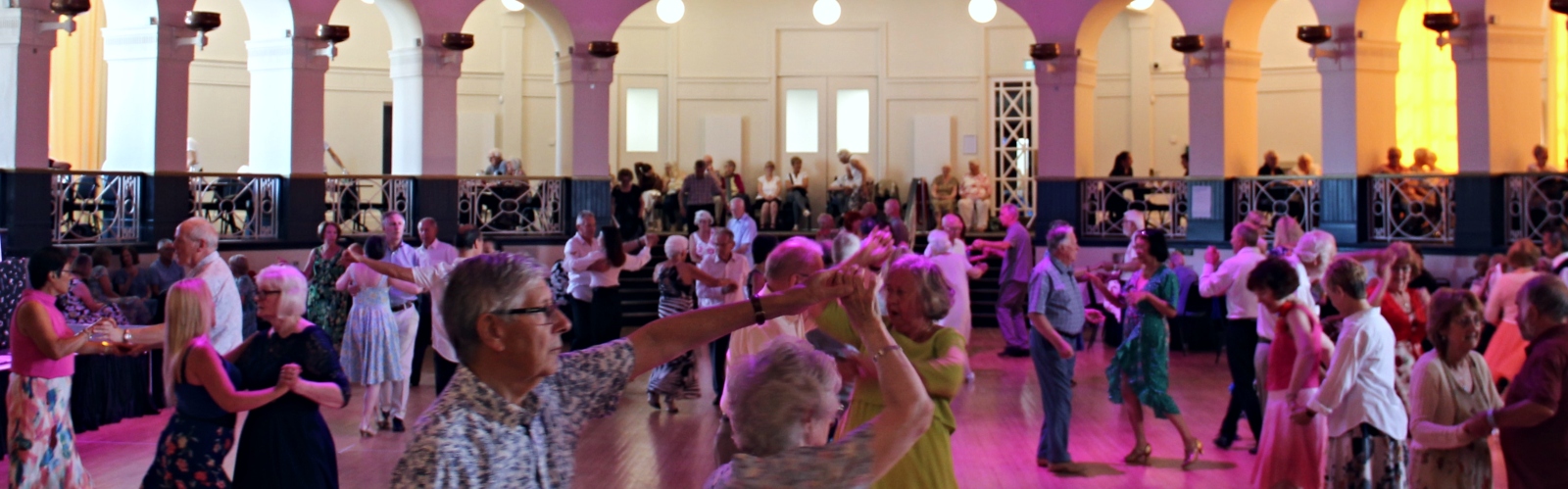 A large group of older people dancing in a grand 1920s ballroom